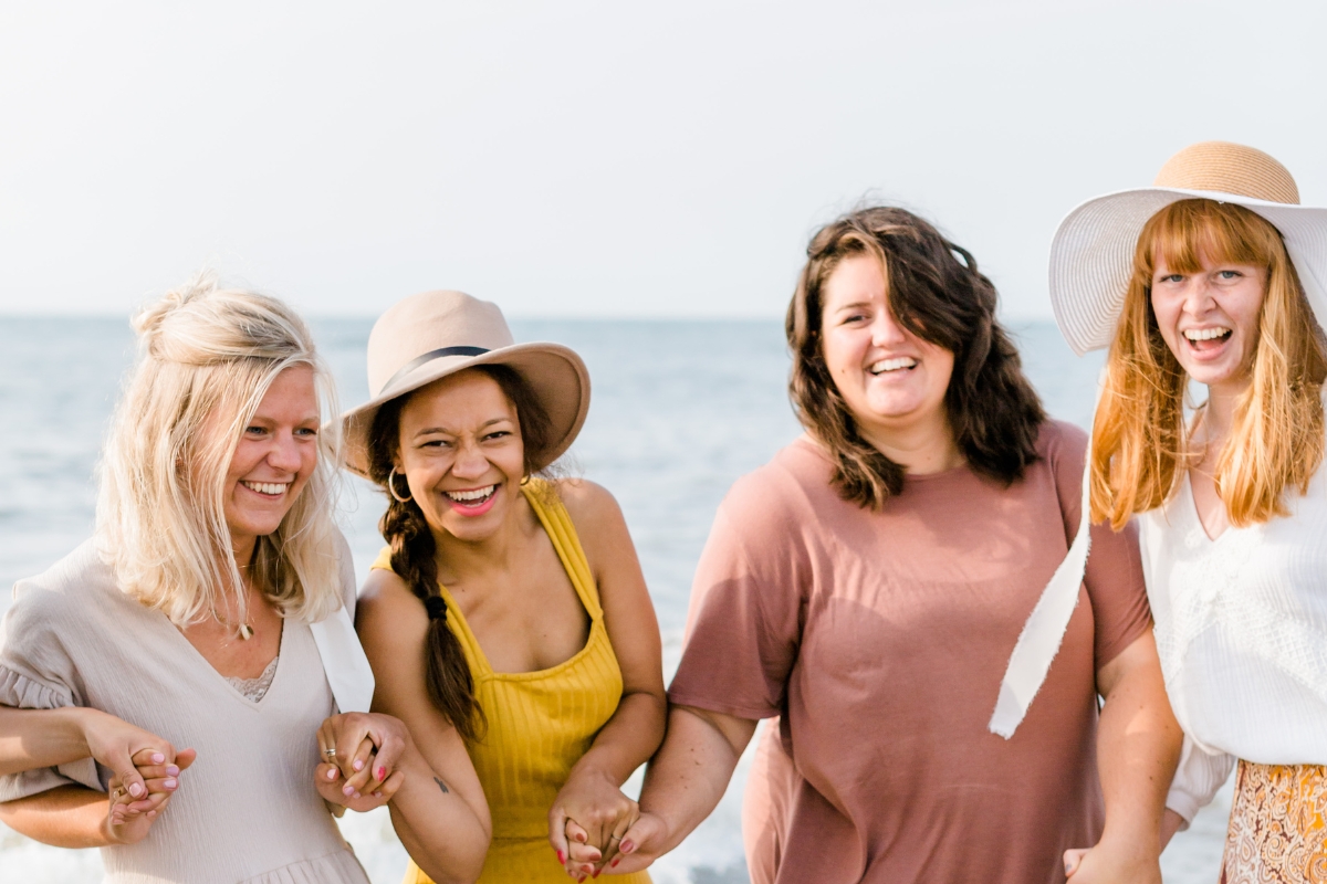 Vier jonge vrouwen houden elkaars handen vast en lachen naar de kijker.